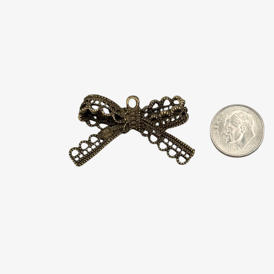 Bronze bow-shaped pendant next to a coin on a white background