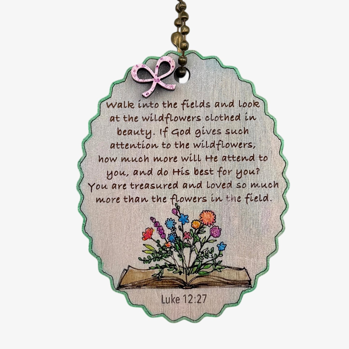 Decorative tag with a quote and illustration of flowers on an open book, featuring Luke 12:27.