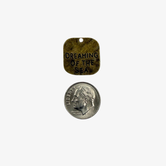 Small metal tag with 'Dreaming of the Sea' text