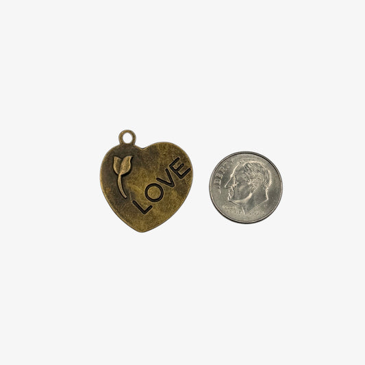 Heart-shaped pendant with 'LOVE' and a tulip design next to a quarter for scale on a white background