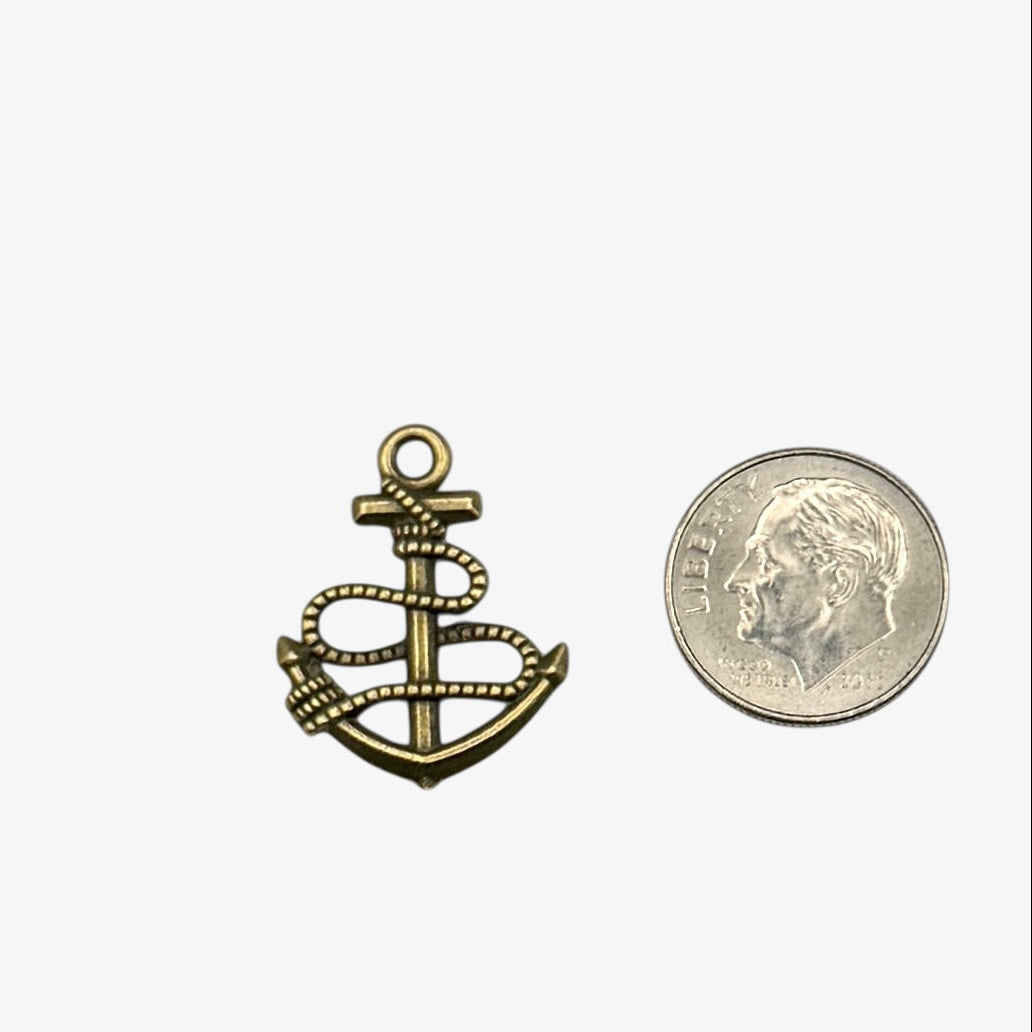 Bronze anchor pendant next to a coin on a white background