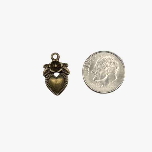 Bronze heart-shaped pendant with floral design next to a quarter on a white background