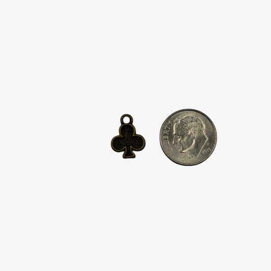 Small black clover charm next to a coin on a white background