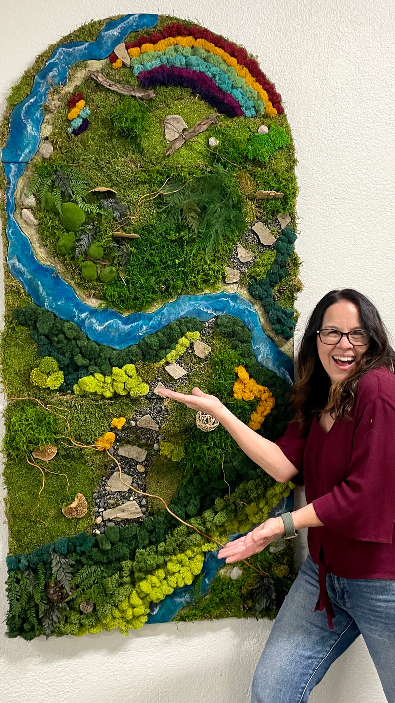 Woman posing with a large, detailed moss wall art piece depicting a landscape with a rainbow.
