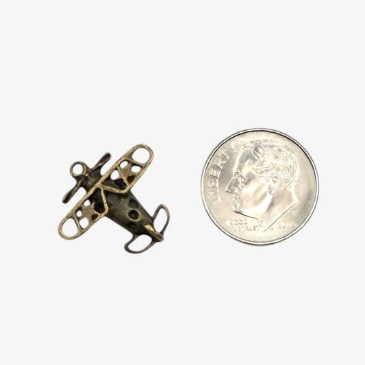 Small bronze airplane charm next to a quarter on a white background