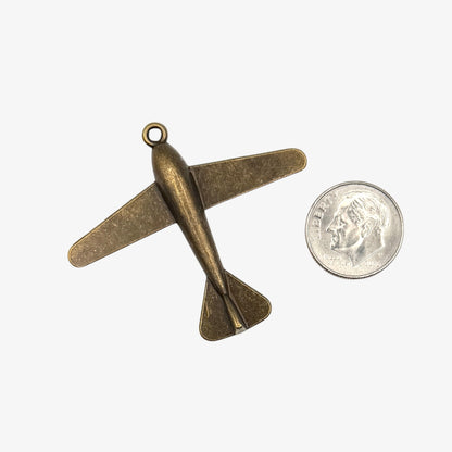 Bronze airplane pendant next to a quarter on a white background