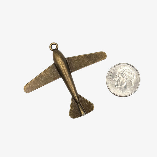 Bronze airplane pendant next to a quarter on a white background