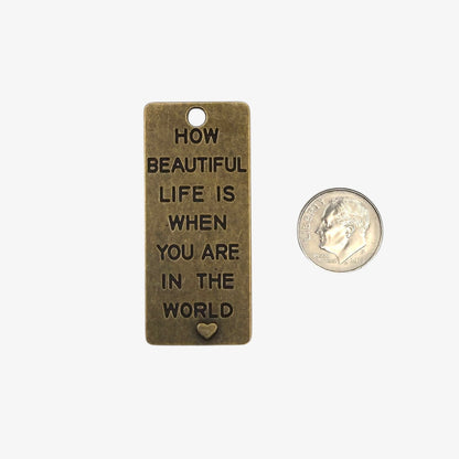 Bronze pendant with engraved text and a heart symbol, next to a quarter for scale on a white background.