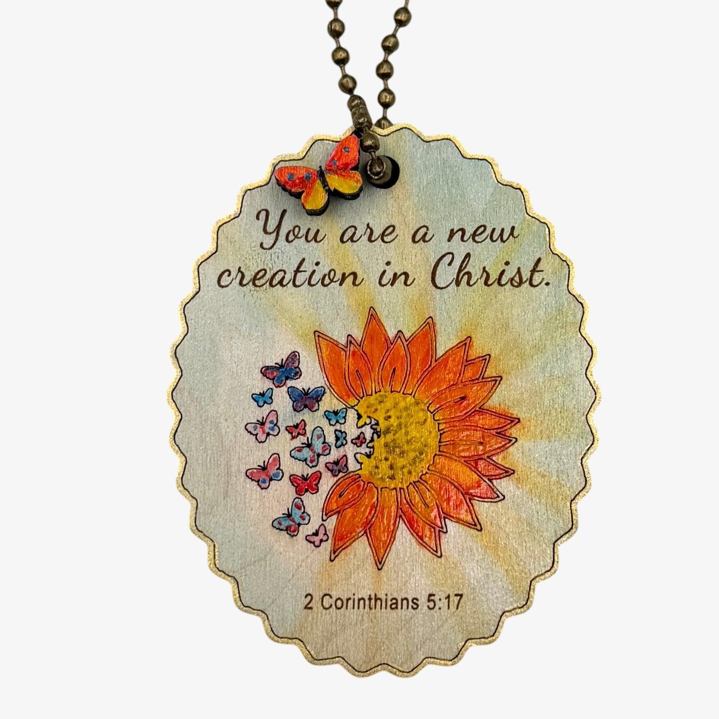 Necklace with pendant featuring a sunflower and butterflies, and text 'You are a new creation in Christ. 2 Corinthians 5:17' on a white background.