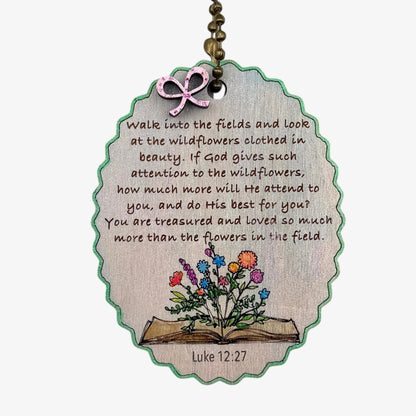 Decorative tag with a quote and illustration of flowers on an open book, featuring Luke 12:27.
