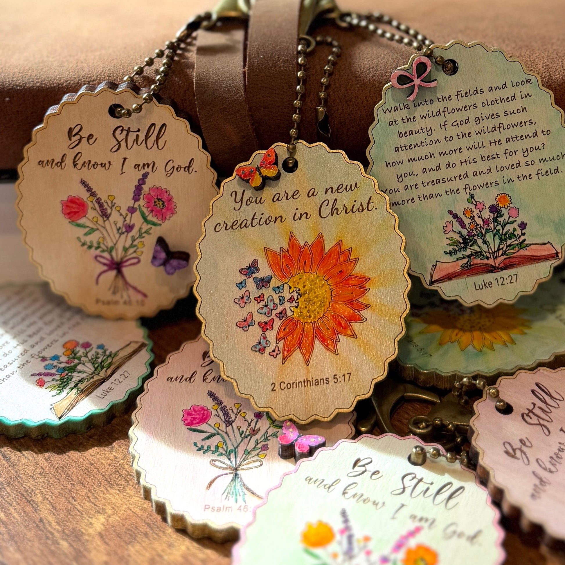 Decorative keychains with floral designs and inspirational text on a wooden surface.