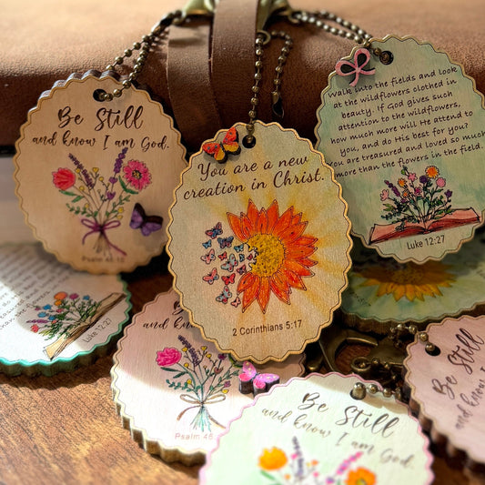 Decorative keychains with floral designs and inspirational text on a wooden surface.