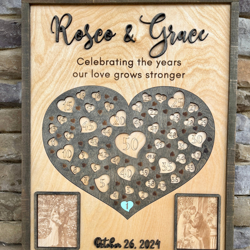 Wooden anniversary plaque with heart design and engraved numbers, framed against a stone wall.