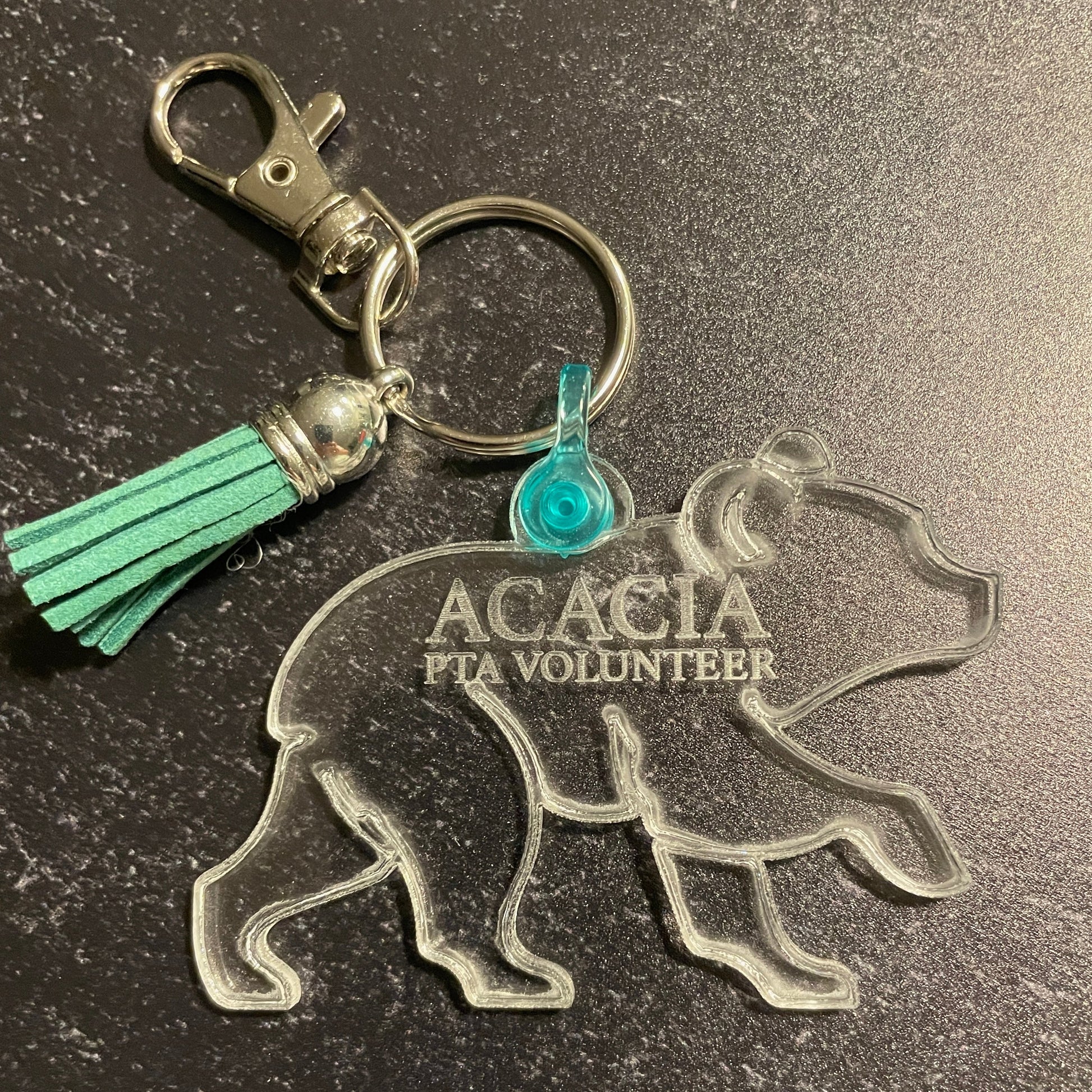 Keychain with bear silhouette and 'Acacia FIA Volunteer' text on a dark surface