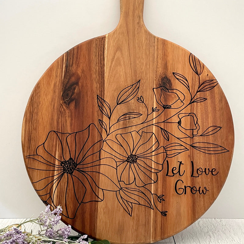 Wooden cutting board with floral design and 'Let love Grow' text on a white background