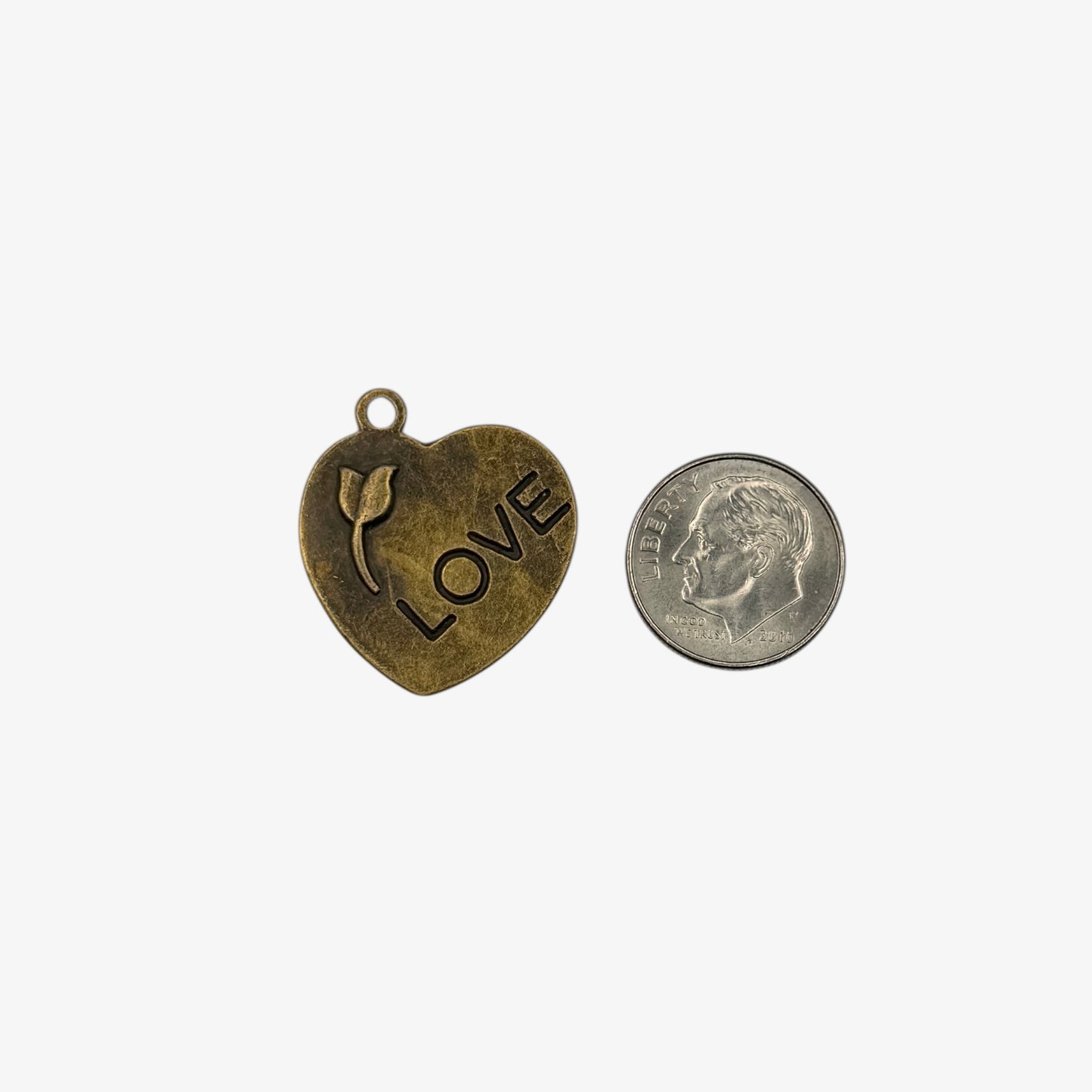 Heart-shaped pendant with 'LOVE' and a tulip design next to a quarter for scale on a white background