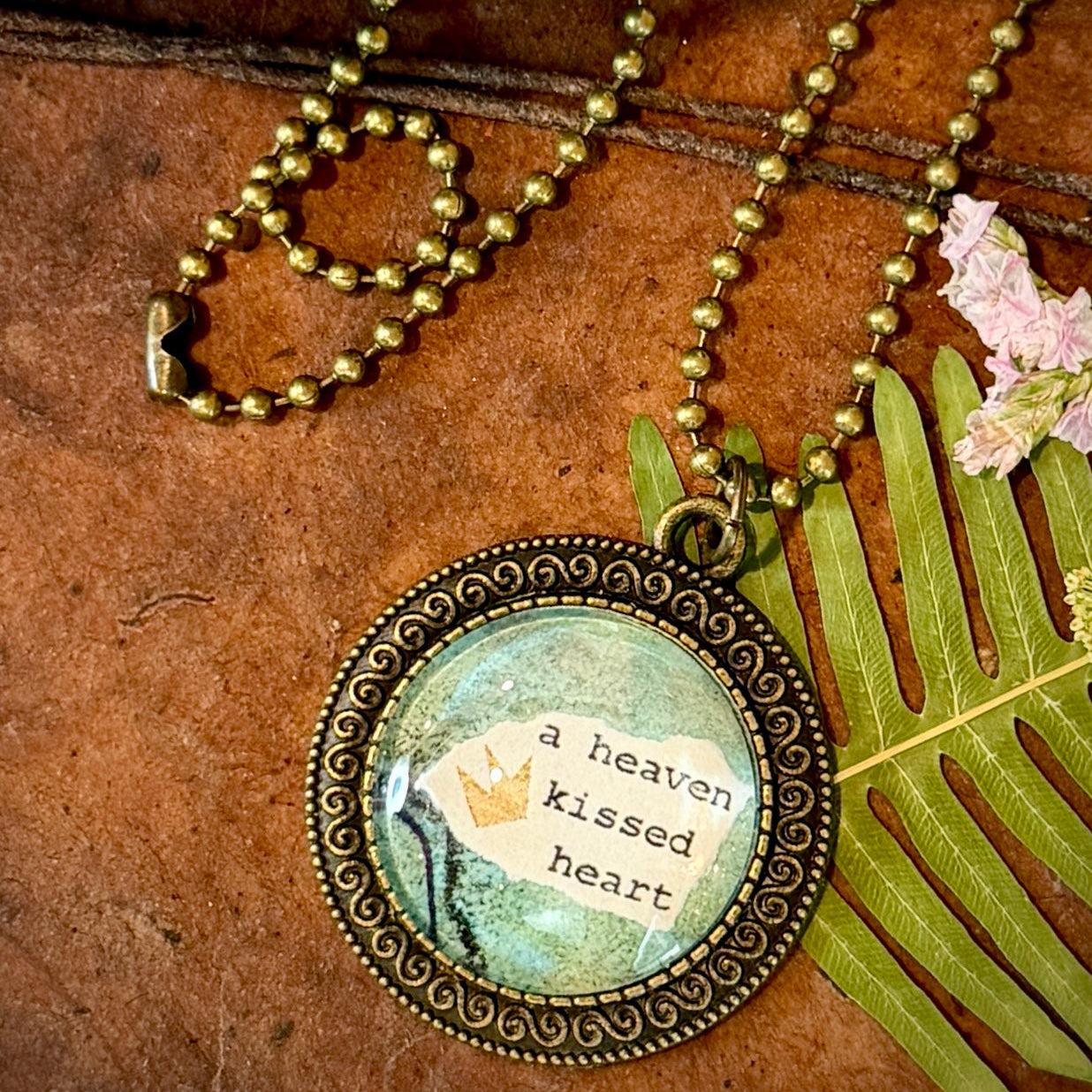 Necklace with a pendant featuring 'a heaven kissed heart' text on a textured surface.