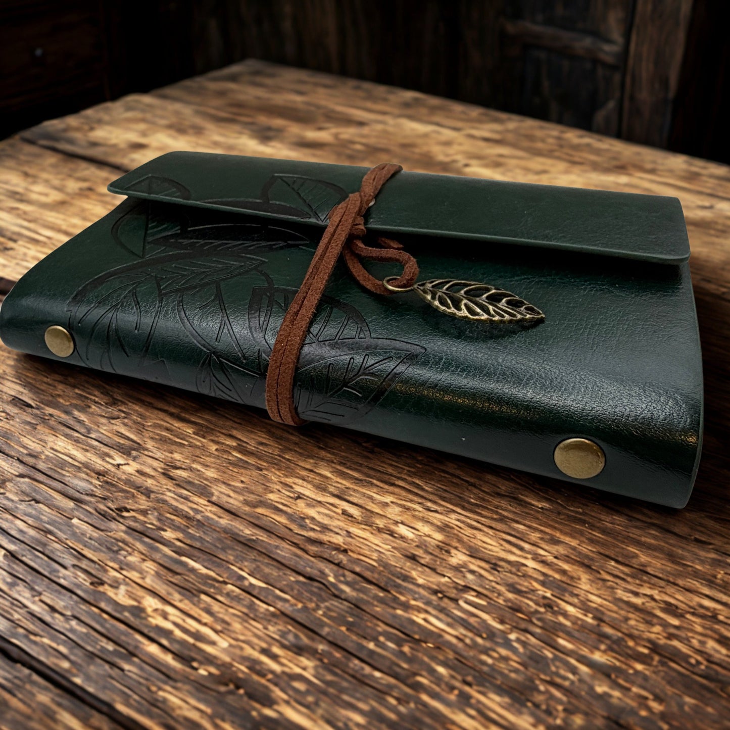 Green leather-bound notebook with a bronze leaf charm on a wooden surface