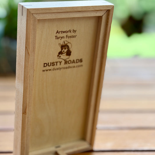 Wooden box with 'Dusty Roads' branding and artist information on a blurred background