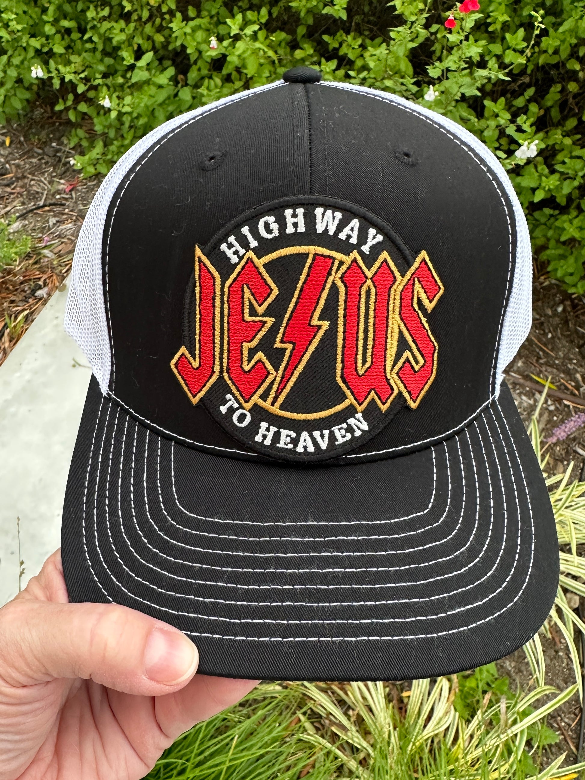 Black and white cap with 'Highway Jesus to Heaven' logo held by a hand against a green background.