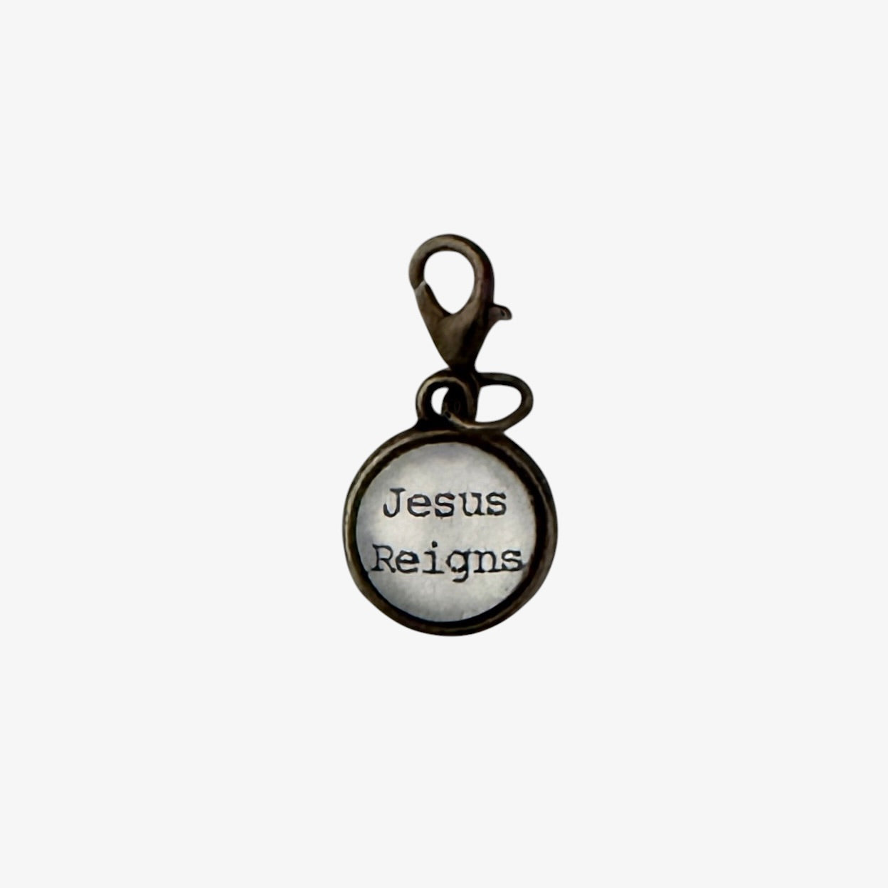 Round metal charm with 'Jesus Reigns' text on a white background