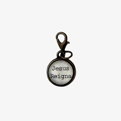 Round metal charm with 'Jesus Reigns' text on a white background