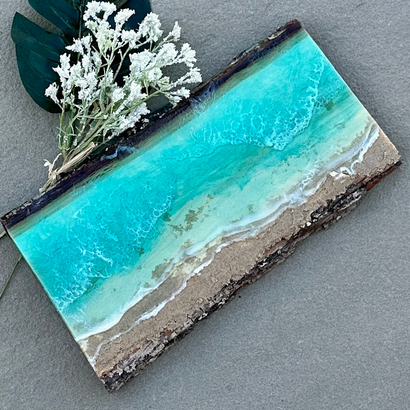 Decorative piece with turquoise water and sand design on a gray surface, accompanied by white flowers.