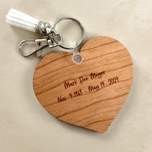 Wooden heart-shaped keychain with engraved text on a beige background