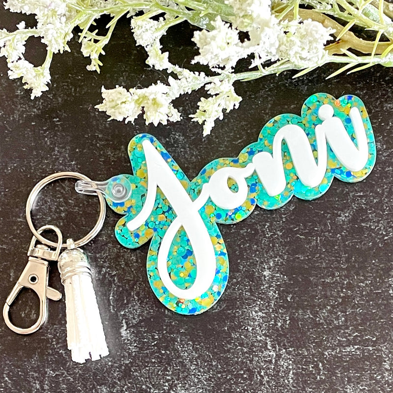 Keychain with floral design and personalized  text on a dark surface with flowers.