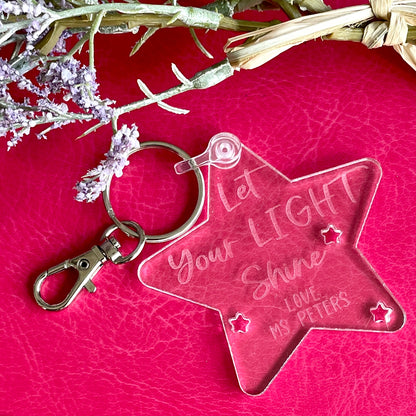 Star-shaped keychain with engraved text on a pink surface with floral elements.