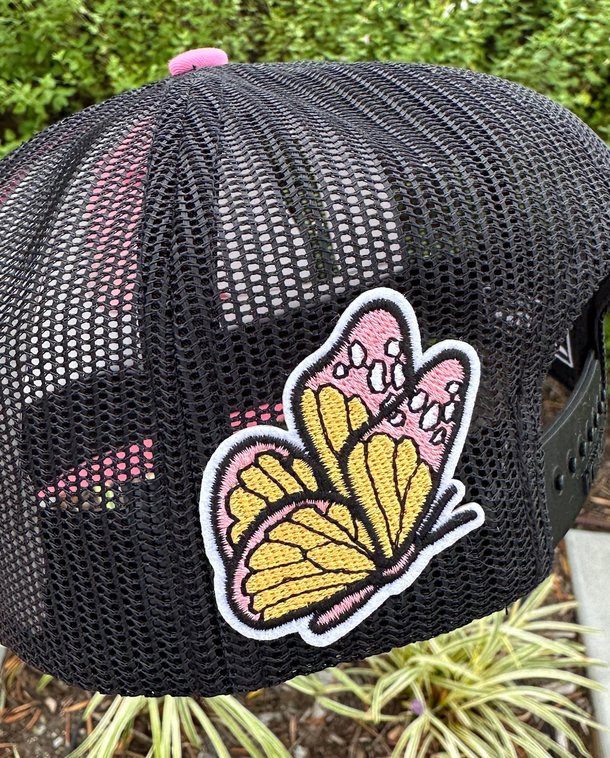 Black mesh cap with a butterfly patch on a blurred natural background