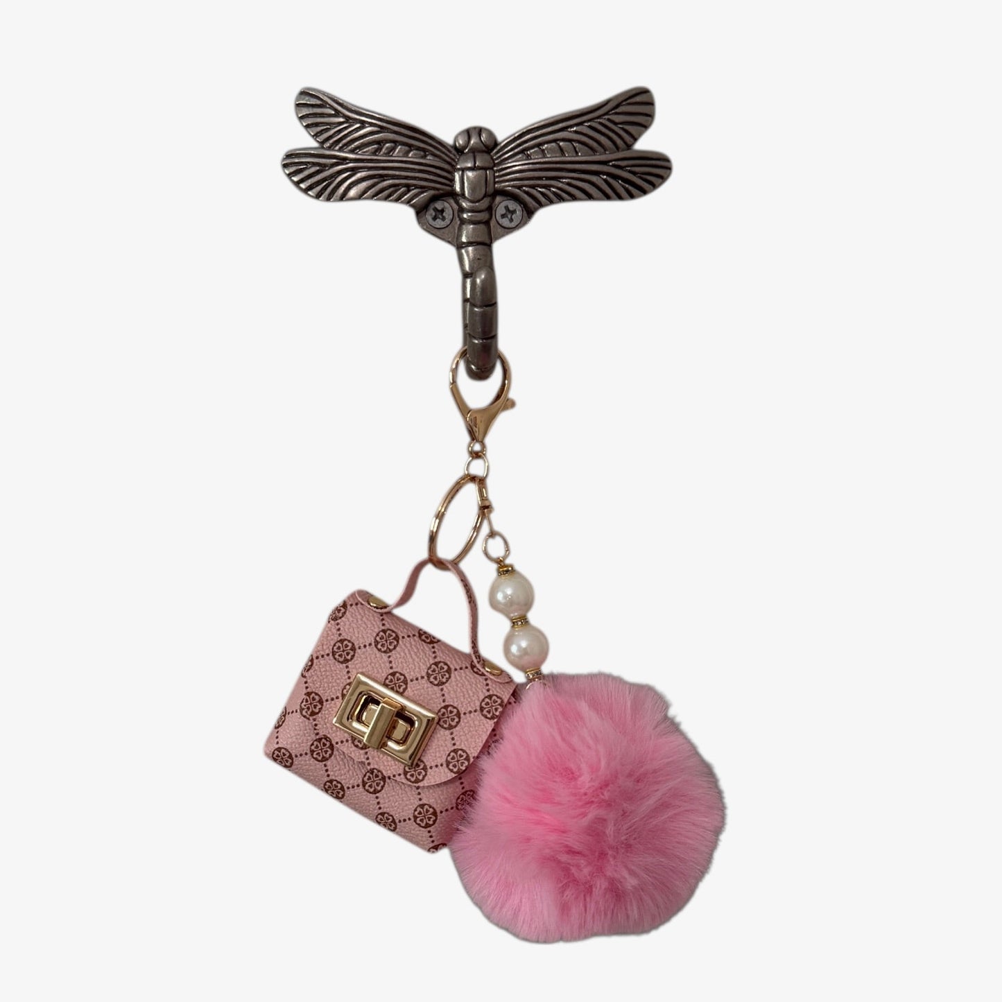Keychain with dragonfly design, pink purse charm, and pink pom-pom on a white background