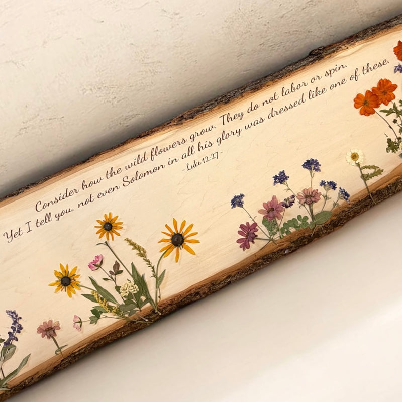 Decorative wooden plaque with pressed flowers and a biblical quote on a neutral background
