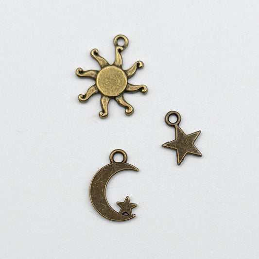 Three metallic charms shaped like a sun, moon, and star on a white background