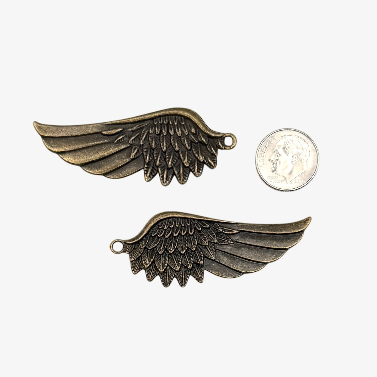 Two bronze wing-shaped pendants next to a quarter for scale on a white background