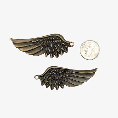 Two bronze wing-shaped pendants next to a quarter for scale on a white background