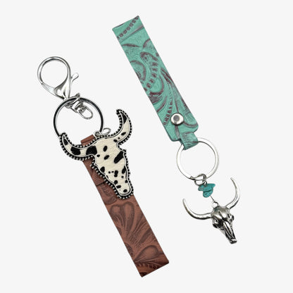 Two keychains with cow skull designs on a white background