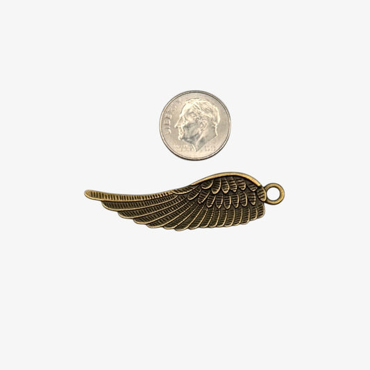 Bronze wing-shaped pendant next to a coin on a white background