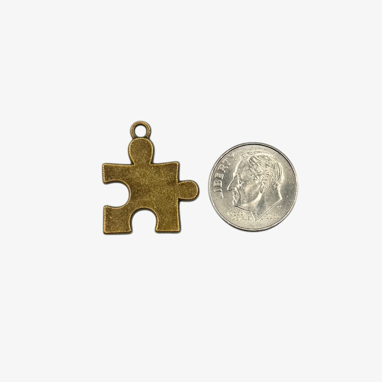 Bronze puzzle piece pendant next to a coin on a white background