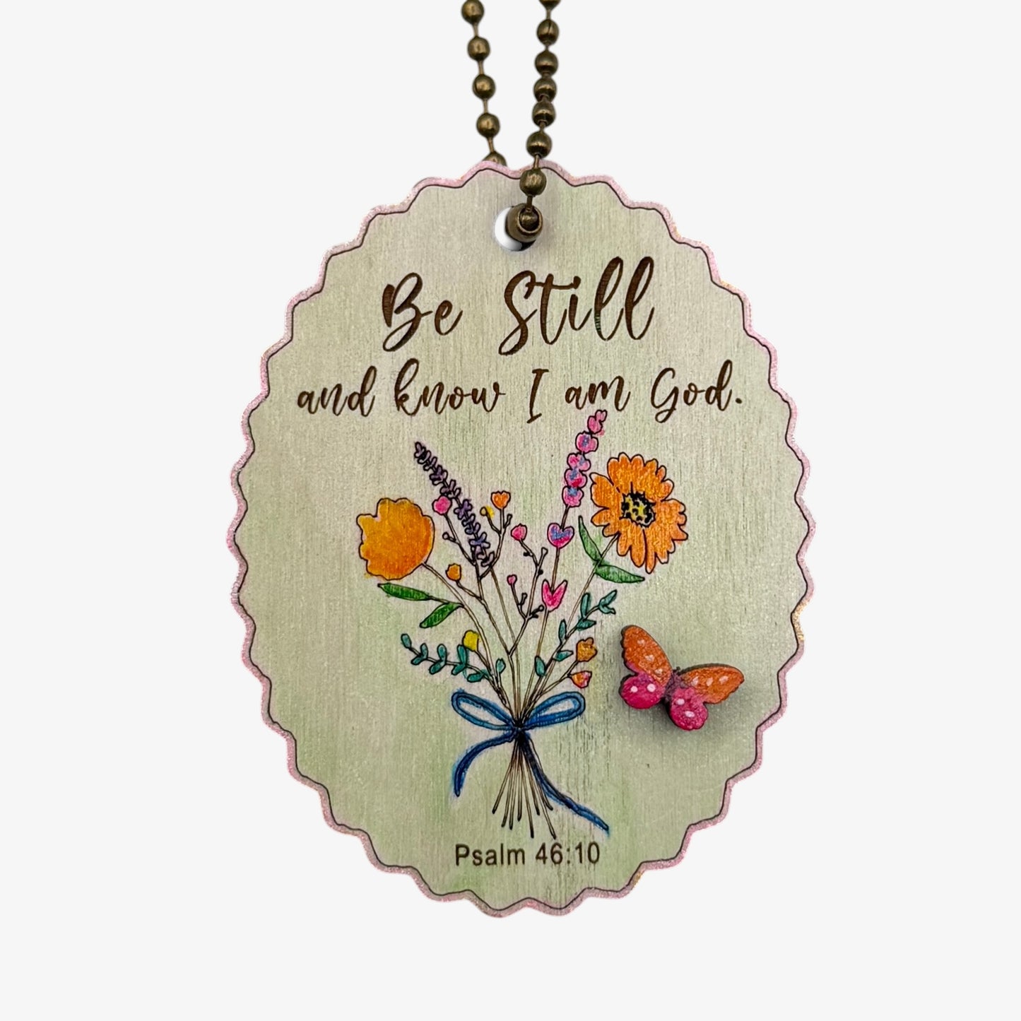 Decorative pendant with floral design and text 'Be Still and know I am God' on a white background