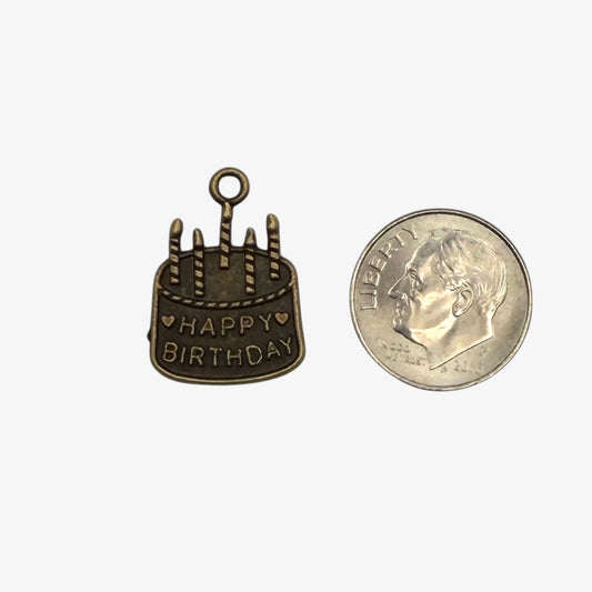 Bronze 'Happy Birthday' cake charm next to a quarter for size comparison on a white background