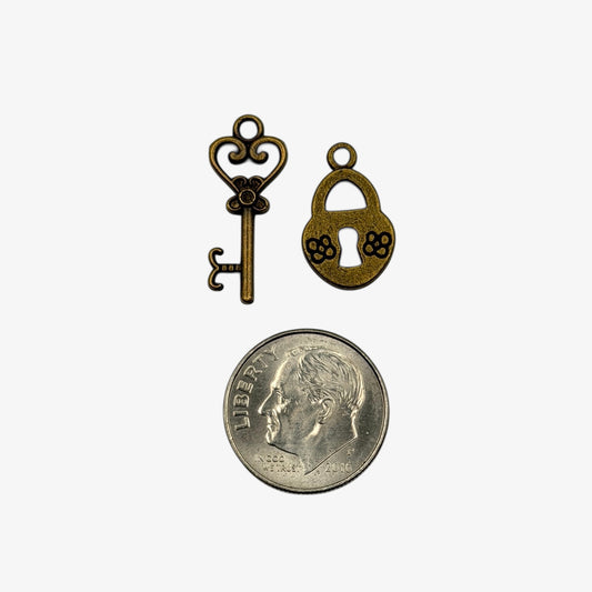 Bronze key and lock charm with a quarter for scale on a white background