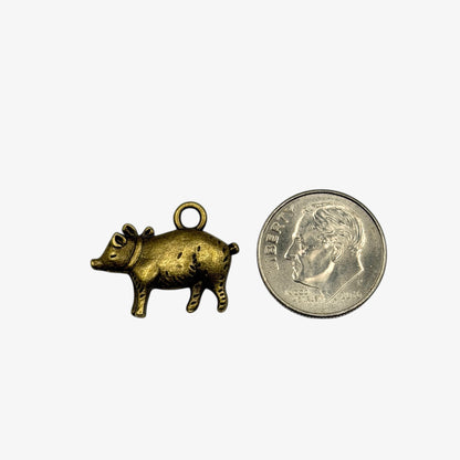 Bronze pig charm next to a quarter on a white background