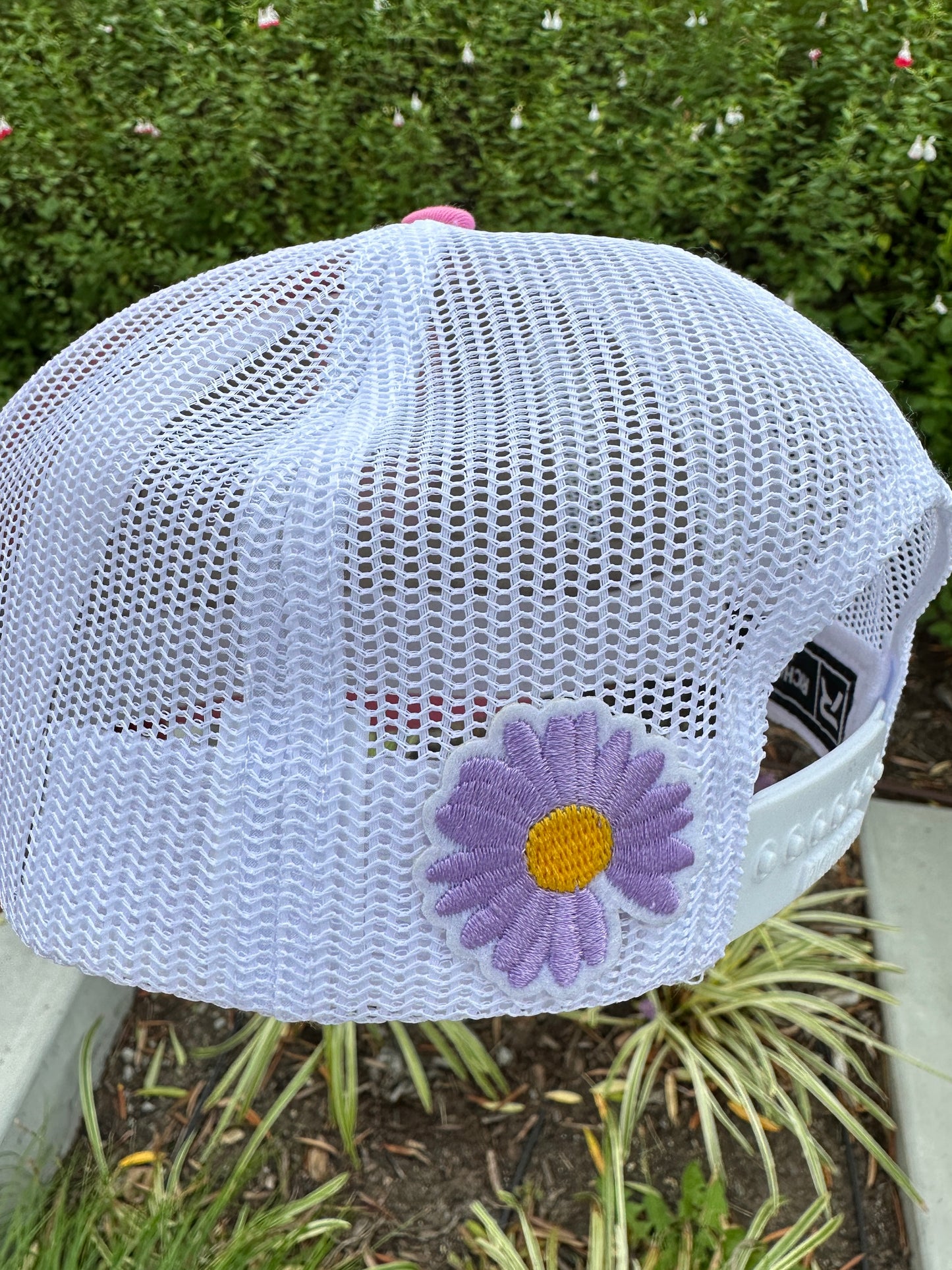 White mesh cap with a purple flower design on a blurred natural background