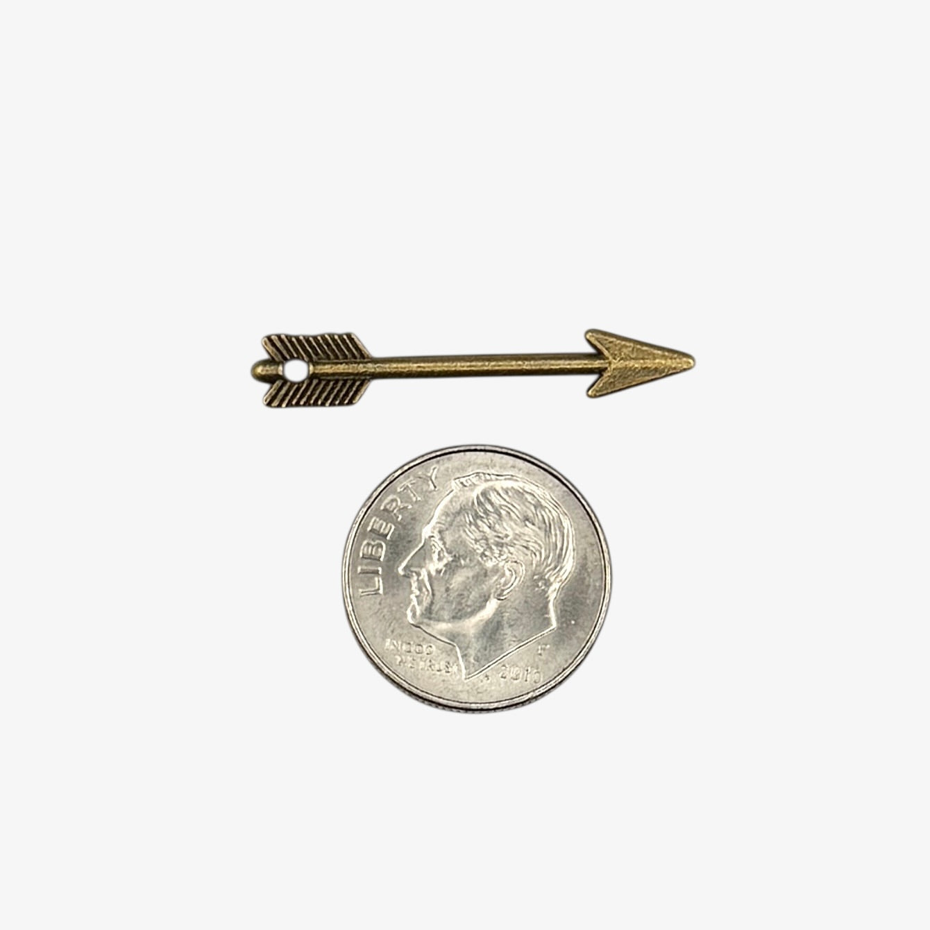 Small bronze arrow-shaped object next to a U.S. quarter coin on a white background