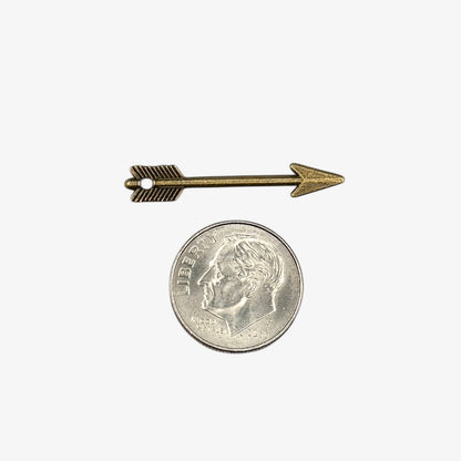 Small bronze arrow-shaped object next to a U.S. quarter coin on a white background