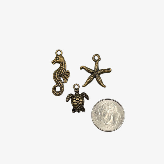 Three bronze-colored charms (seahorse, turtle, and starfish) next to a coin on a white background