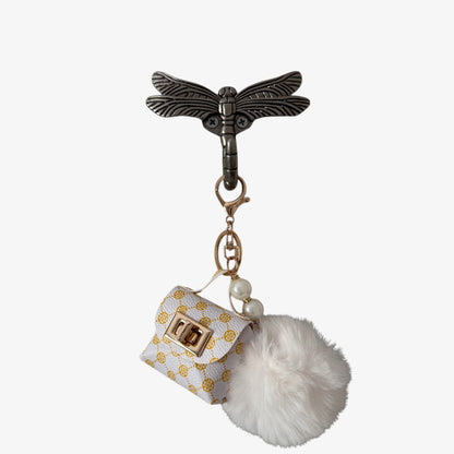 Keychain with dragonfly design, small bag charm, and white pom-pom on a white background